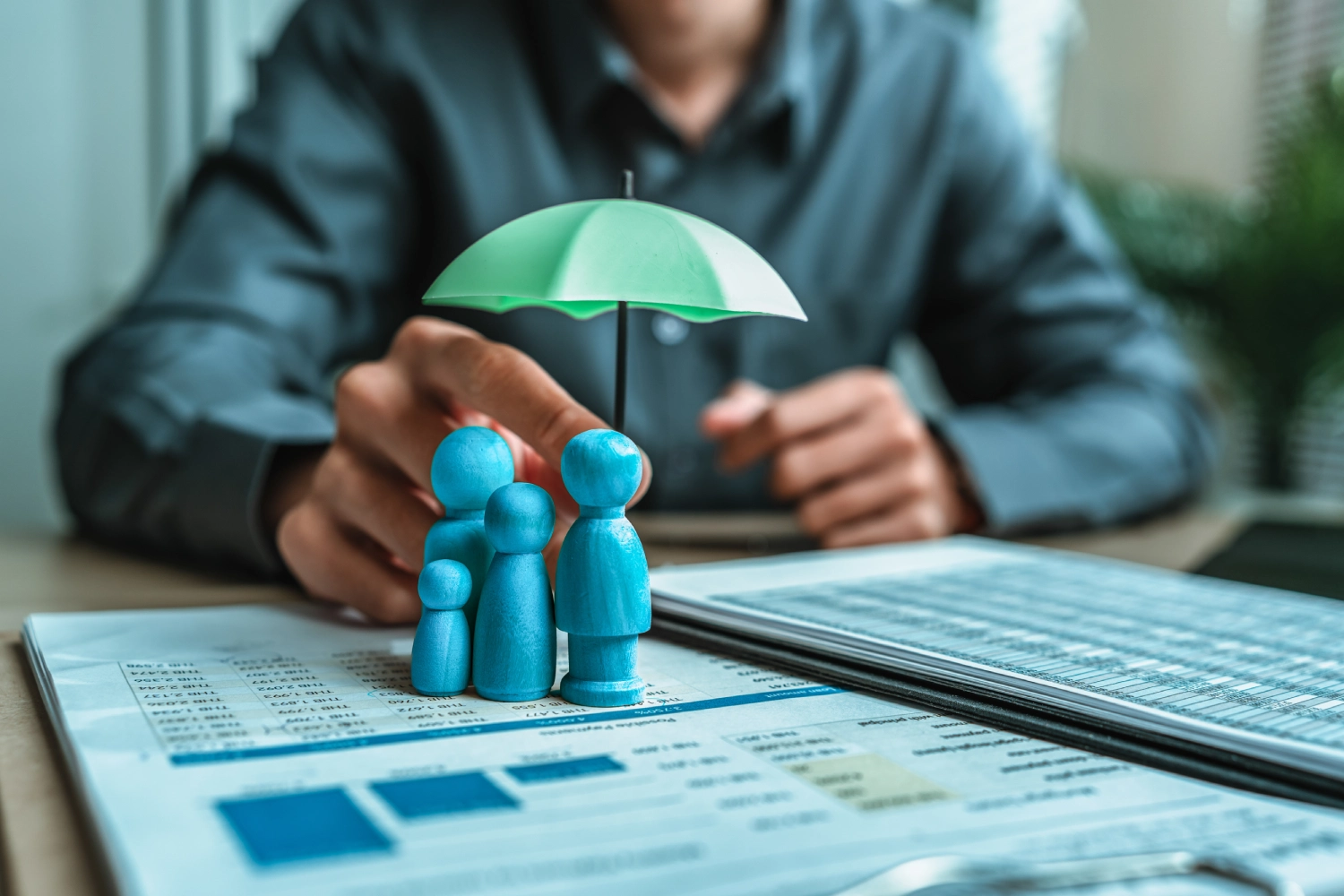 A hand holding a green umbrella over blue family figures symbolizing protection.