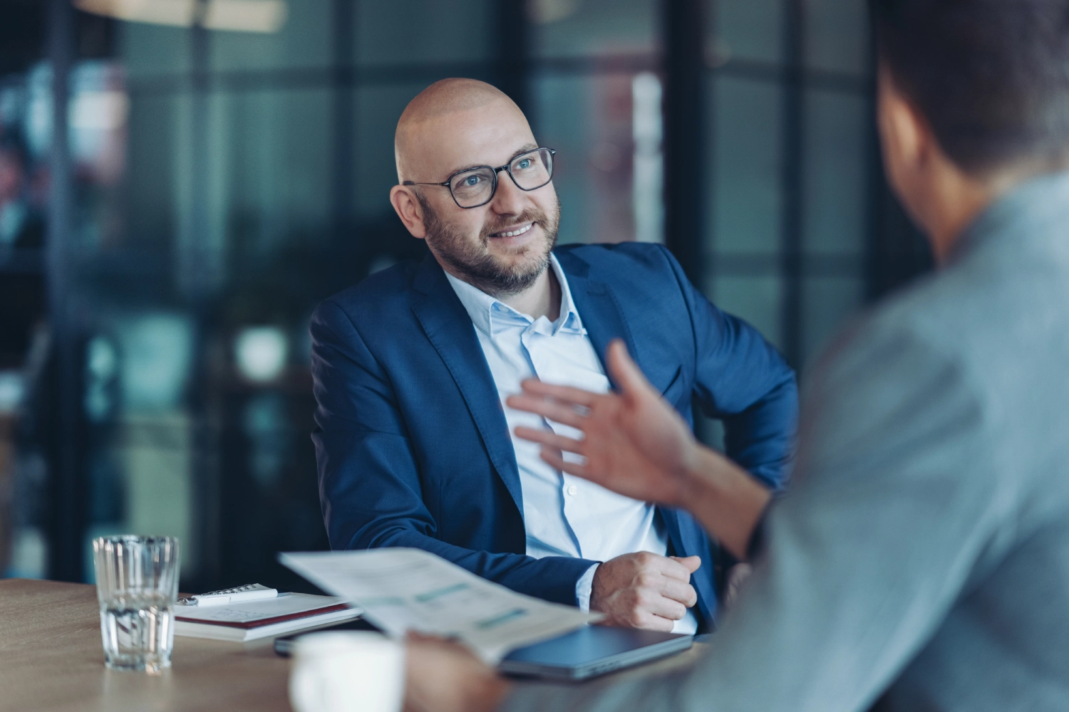 A man in a blue blazer engaged in a conversation during a meeting.