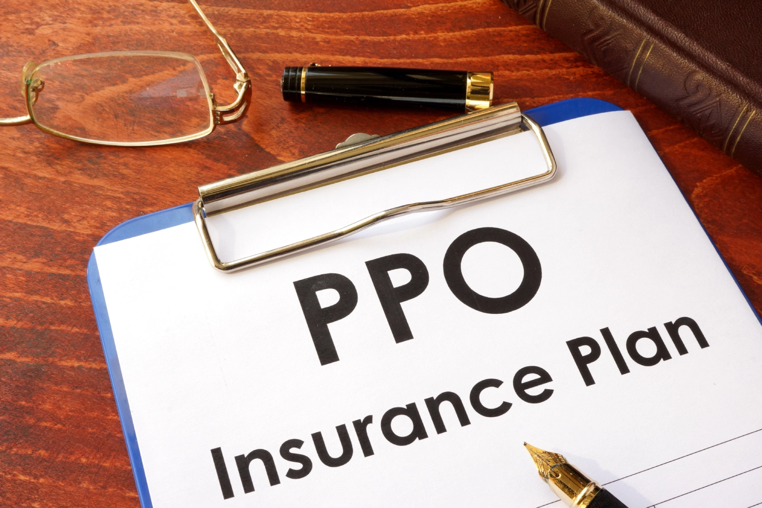 A PPO insurance plan document on a clipboard with a pen and glasses nearby.